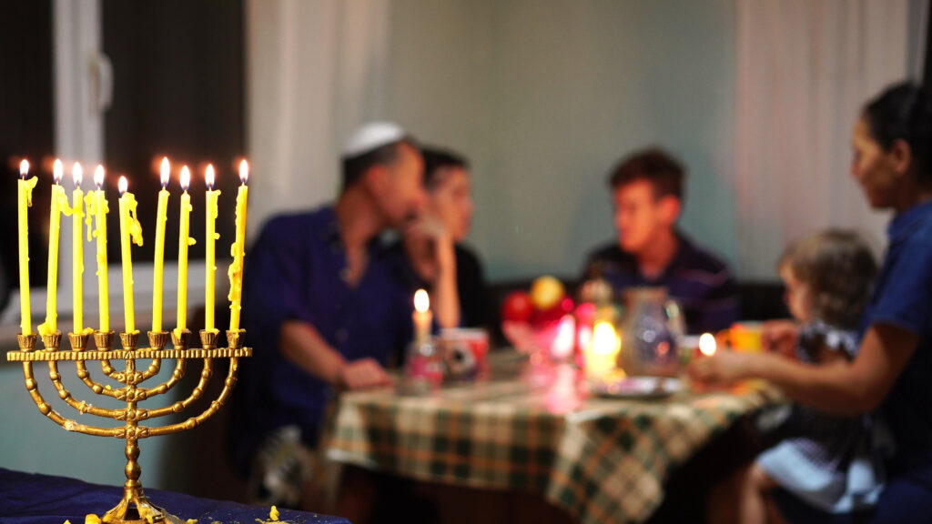 a jewish family enjoying a meal together. a lit menorah is in the foreground.