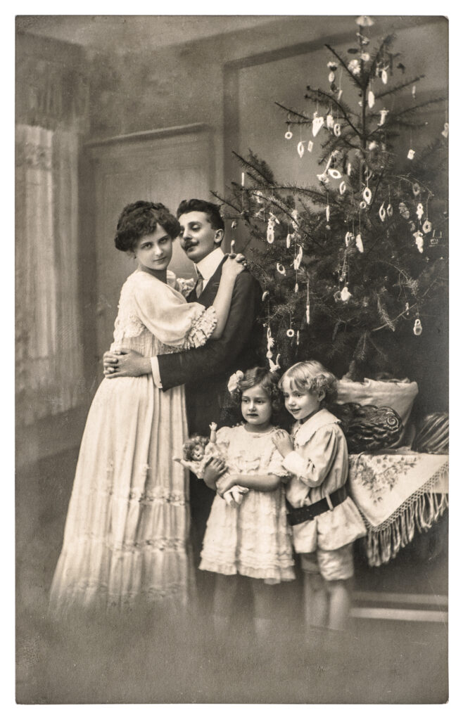 a black and white photograph of a victorian family standing in front of a lightly decorated christmas tree