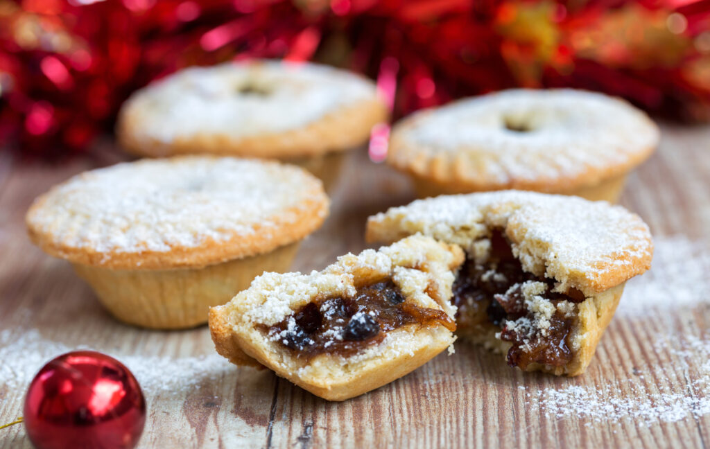 four mince pies. one has been cut in half to show the mincemeat filling