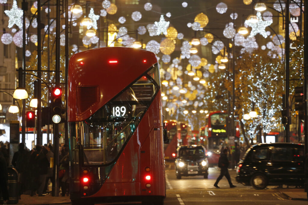 A red london bus driving down Oxford street lit with christmas lights
