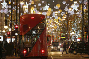 A red london bus driving down Oxford street lit with christmas lights