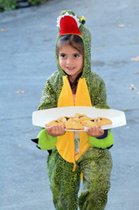 a girl dressed as a dinosaur for purim holding a plate of traditional hanamtaschen pastries